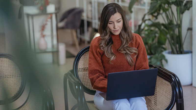 woman sitting on a black rattan chair with a laptop